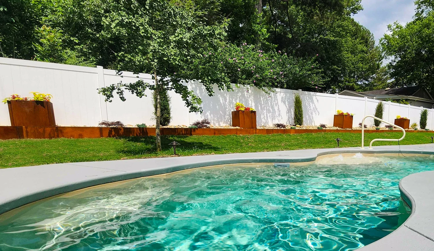 Backyard pool with lush garden and white fence.