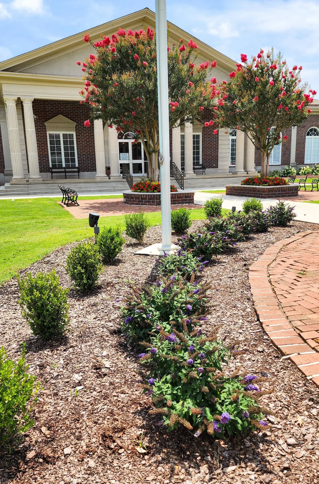 Building entrance with colorful flowers and bushes.
