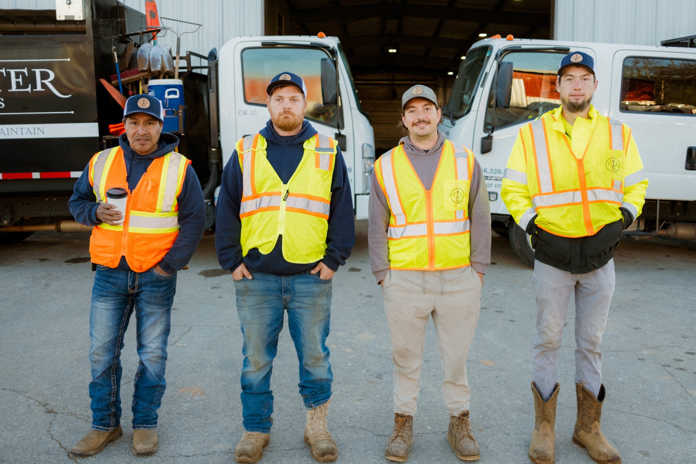Four workers in safety vests by trucks.