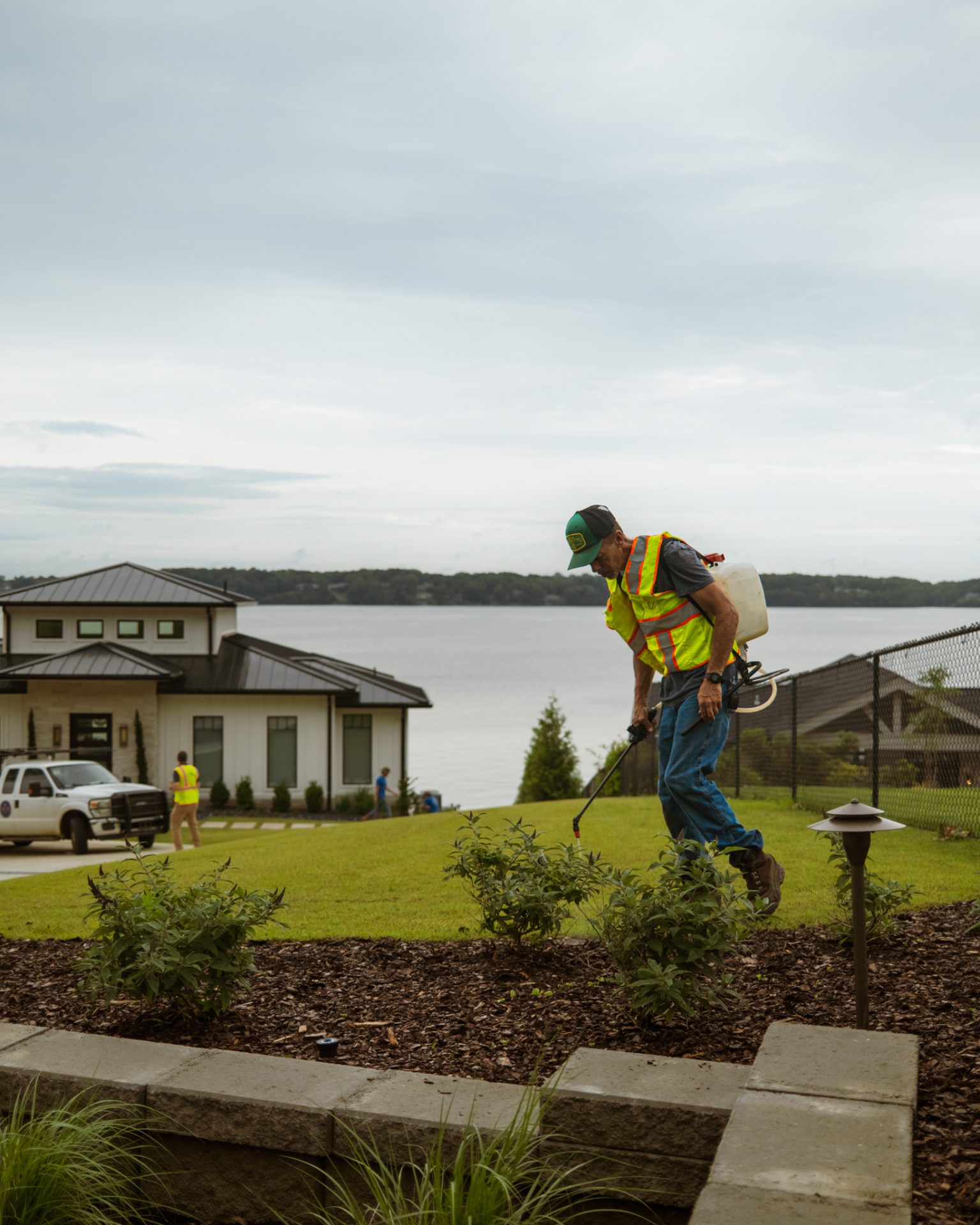 Worker spraying plants near a lakeside house