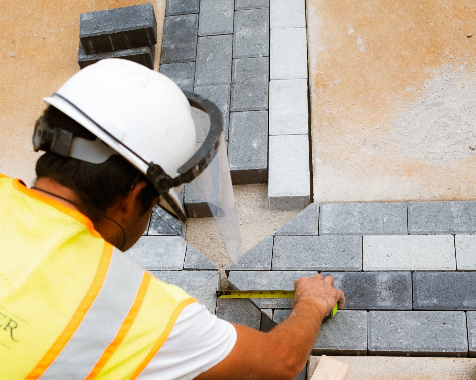 A landscape contractor measuring concrete paver stones with a tape measure during a custom patio installation.