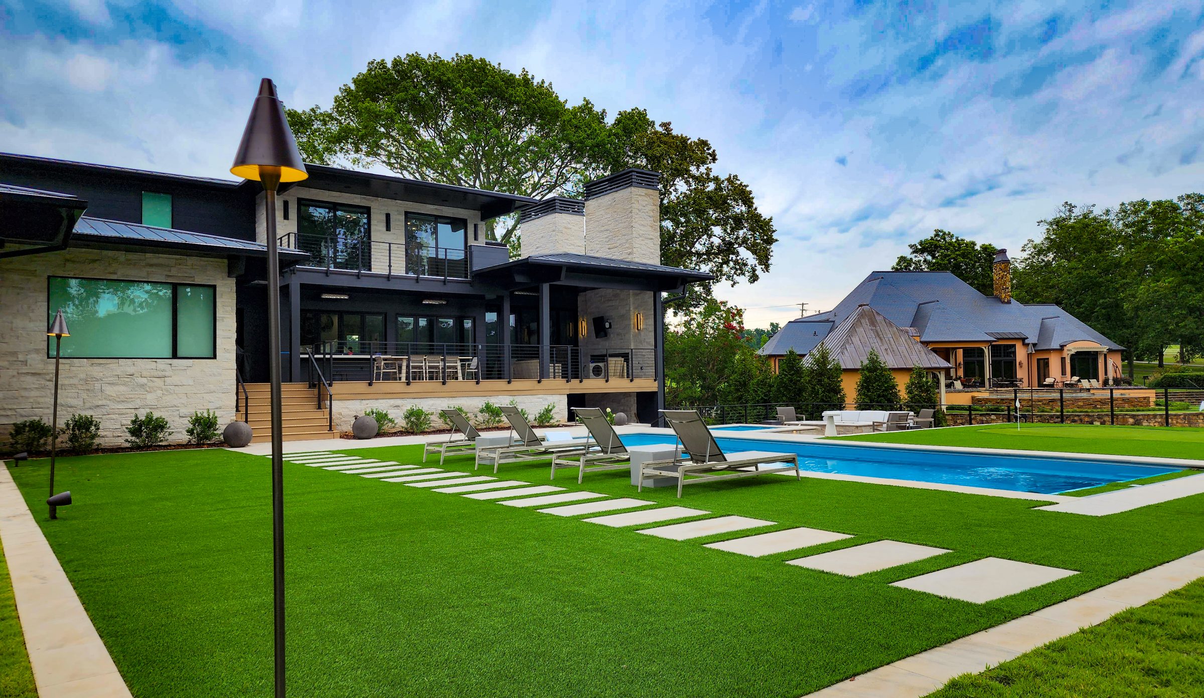 Modern custom hardscape and landscape design featuring a luxury pool, patio pavers, and artificial turf in North Alabama.