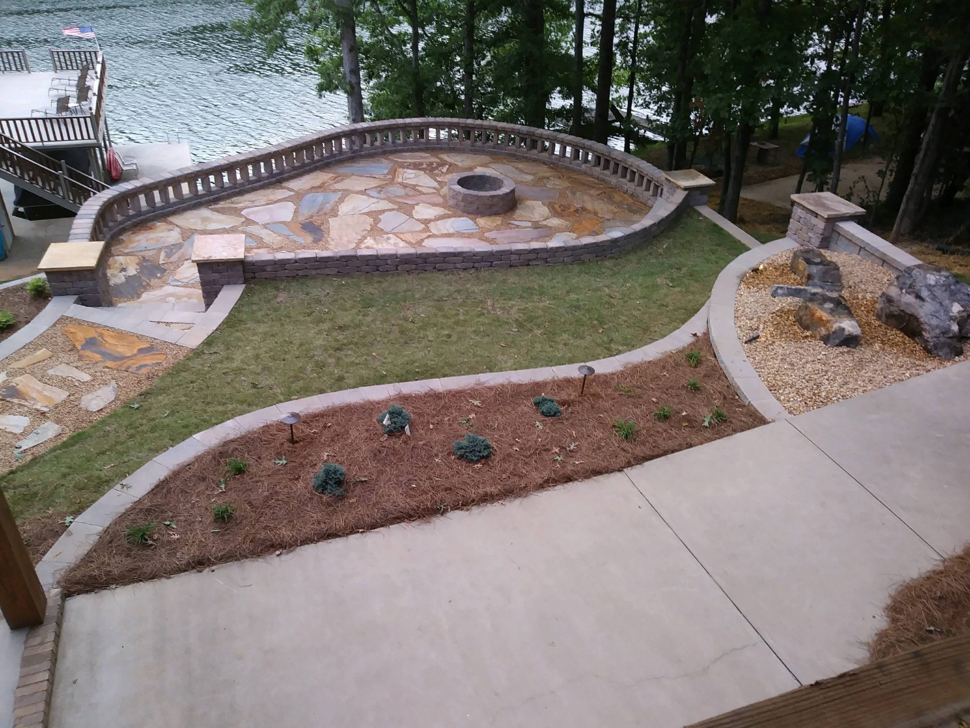 Terraced lakeside backyard featuring a stone fire pit patio, curved retaining walls, and custom rock landscaping.
